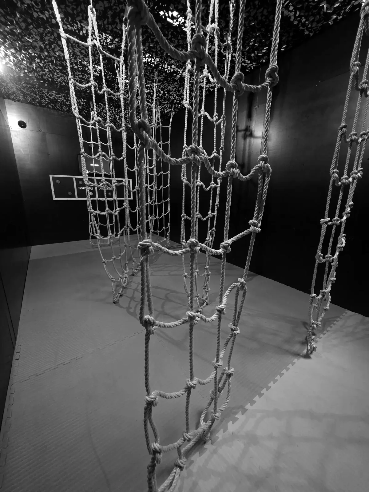 Des filets de corde tendus au-dessus d'un tapis, sur le parcours de Défis Pirate Perpignan, en noir et blanc