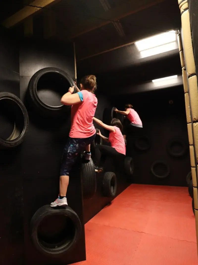Trois joueuses avancent de pneu en pneu le long d'un mur, un défi d'agilité