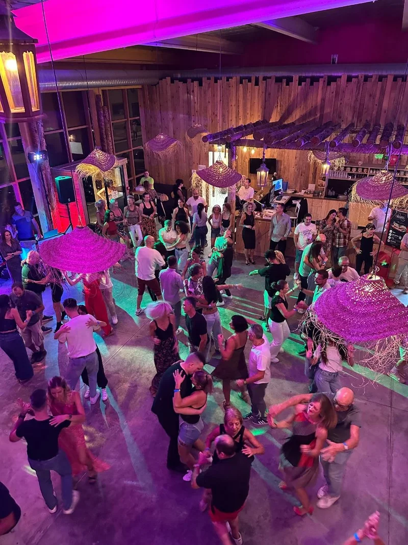 Des couples dansent la bachata dans la grande salle de Défis Pirate Perpignan, sous les lumières violettes et les lampes en paille