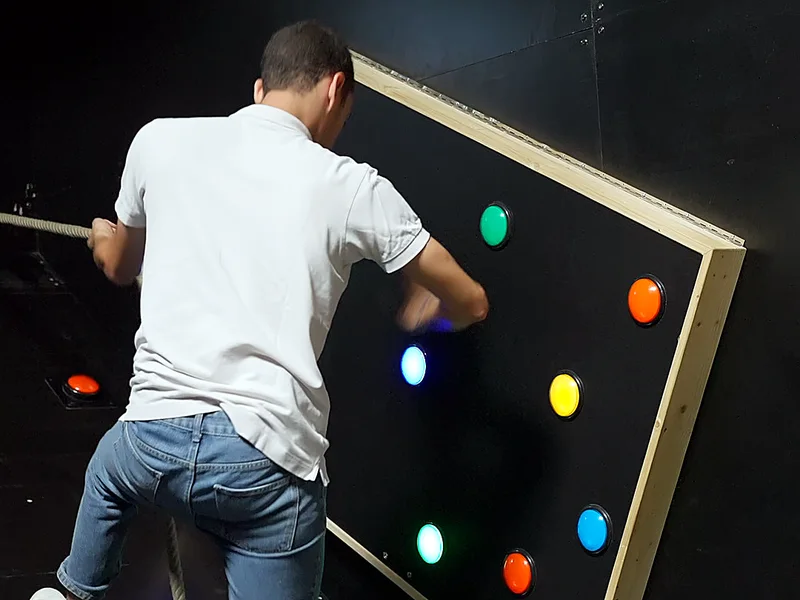 Un joueur, de dos, appuie sur les boutons lumineux d'un mur de défi chez Défis Pirate Perpignan