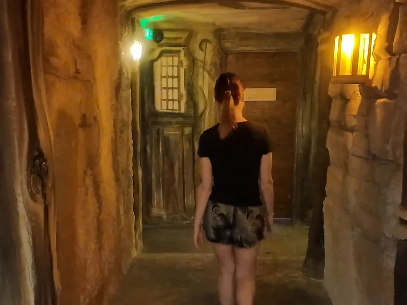 Une joueuse, de dos, avance dans un couloir de pierre éclairé par des lanternes