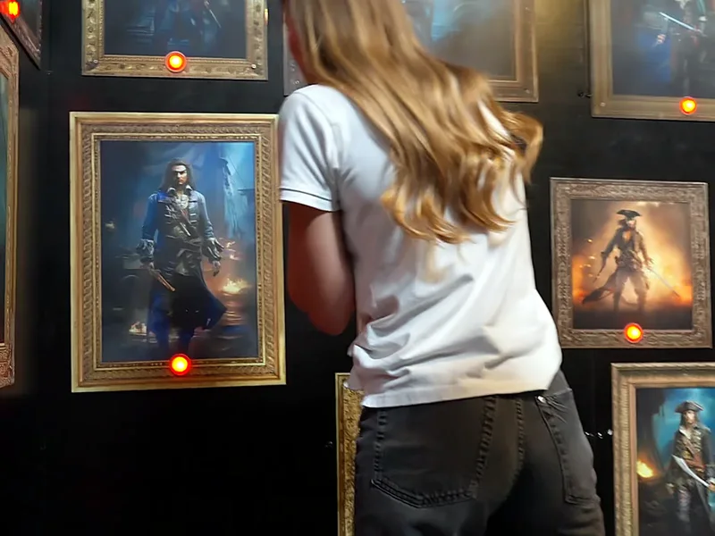 Une joueuse, de dos, observe les portraits de pirates encadrés de la salle des portraits