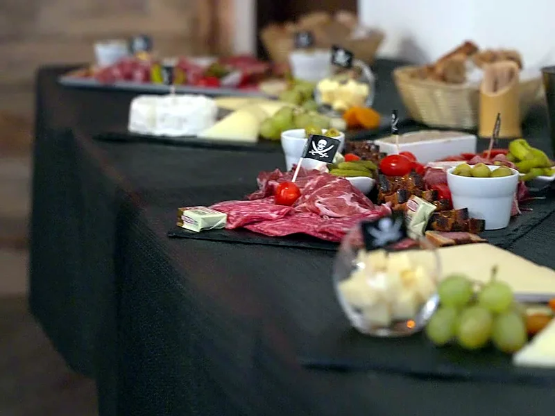 Un buffet de charcuterie, fromages et raisin sur nappe noire, avec des drapeaux pirates