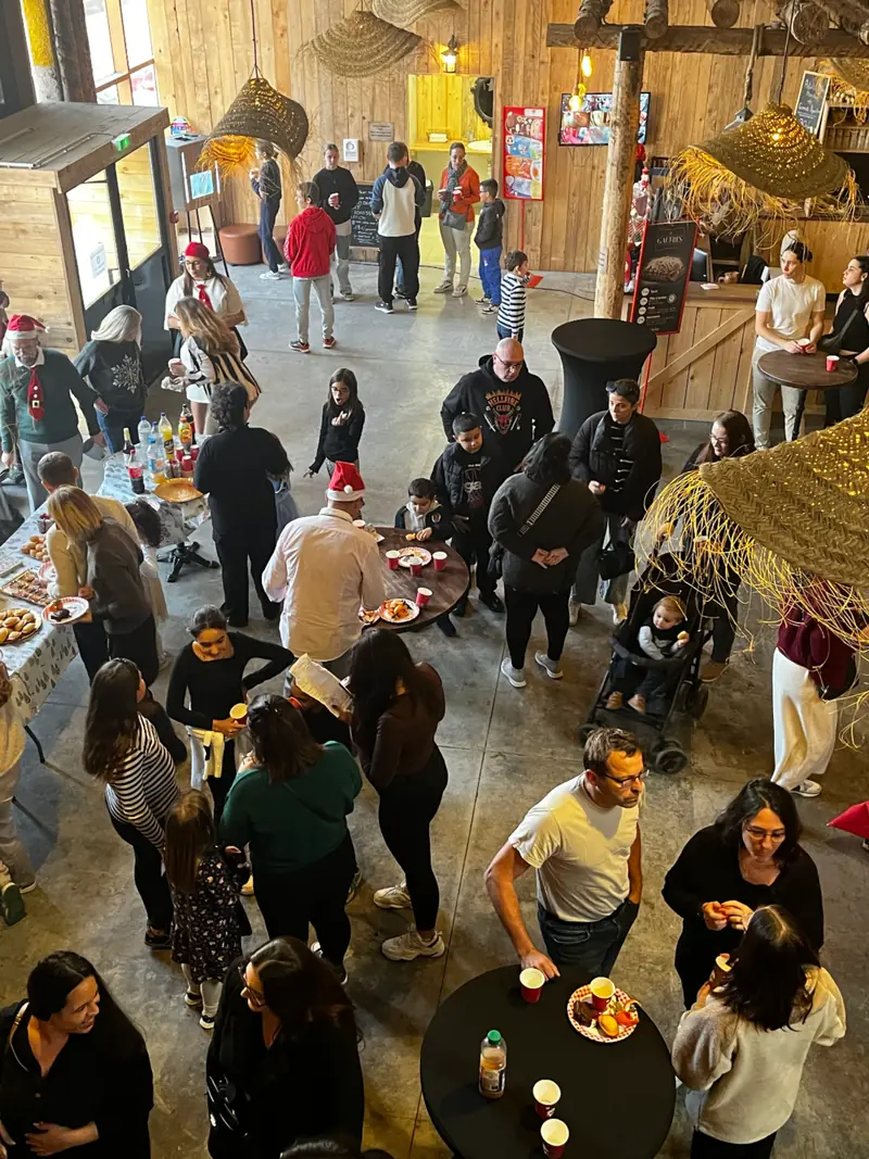Salariés et familles réunis autour des tables hautes lors d'un arbre de Noël chez Défis Pirate, vus depuis la mezzanine