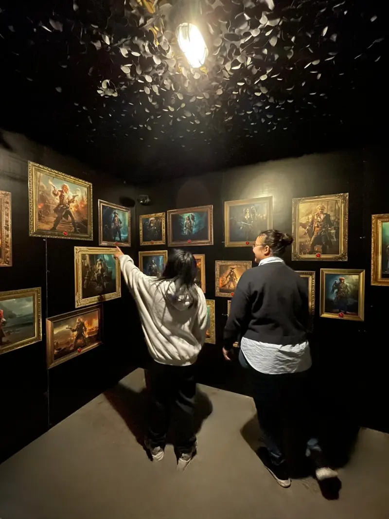 Réflexion : deux joueuses observent une salle de tableaux de pirates