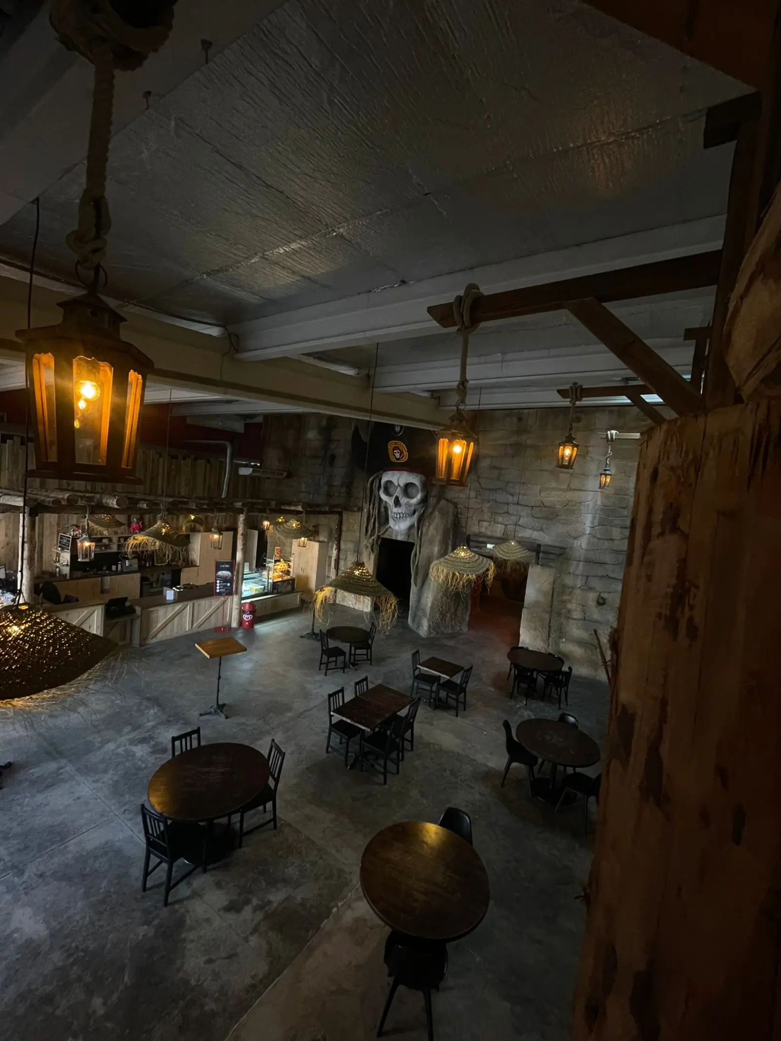 L'espace restauration de Défis Pirate vu d'en haut : tables rondes en bois, lanternes et comptoirs