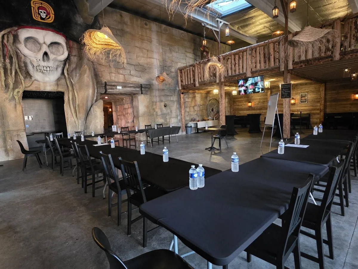La salle de séminaire de Défis Pirate Perpignan, tables dressées sous le crâne pirate géant et la mezzanine en bois