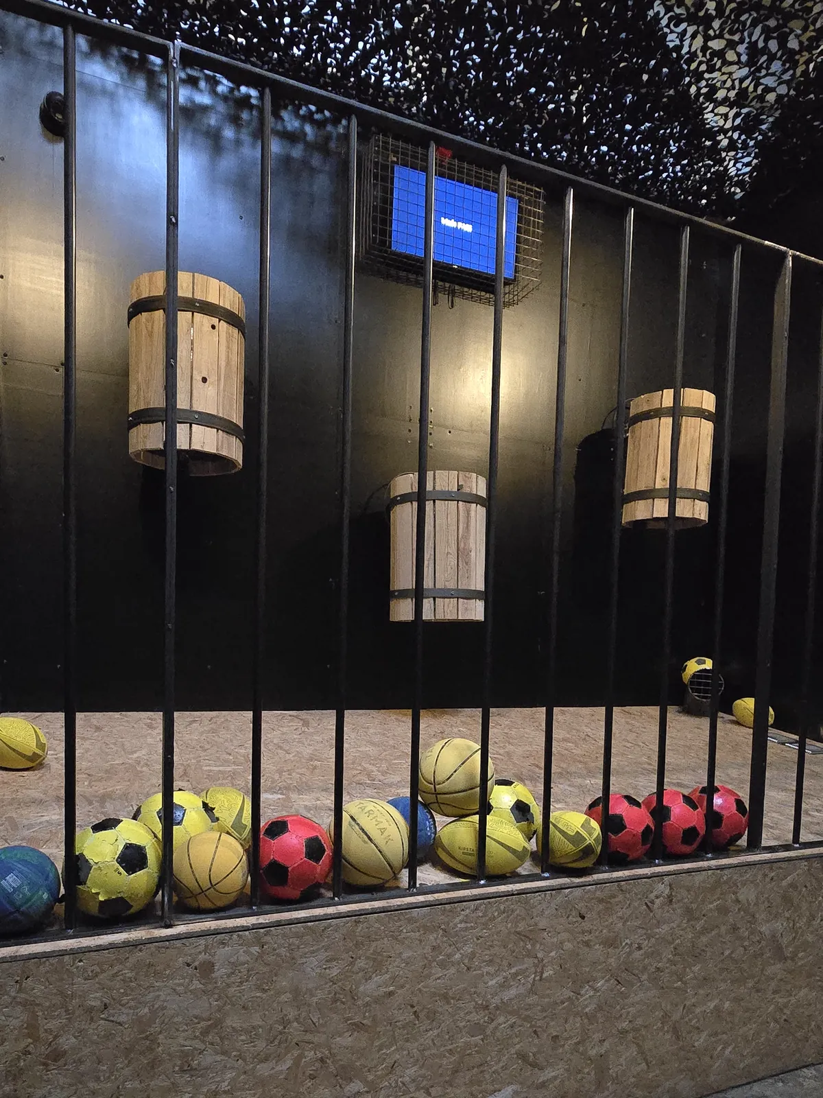 Une salle de défis d'adresse de Défis Pirate Perpignan : des tonneaux suspendus derrière des barreaux, des ballons alignés au sol