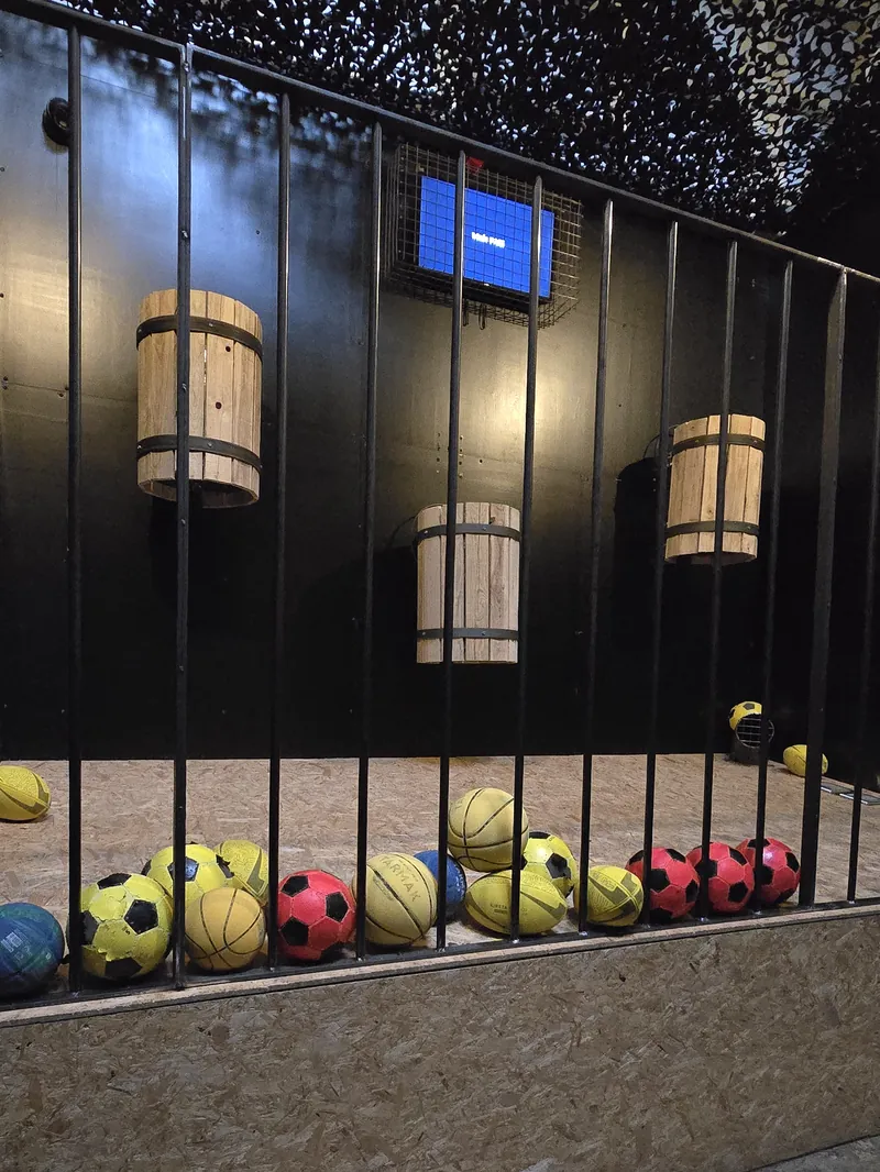 Une salle de défis d'adresse : des tonneaux suspendus derrière des barreaux, des ballons alignés au sol
